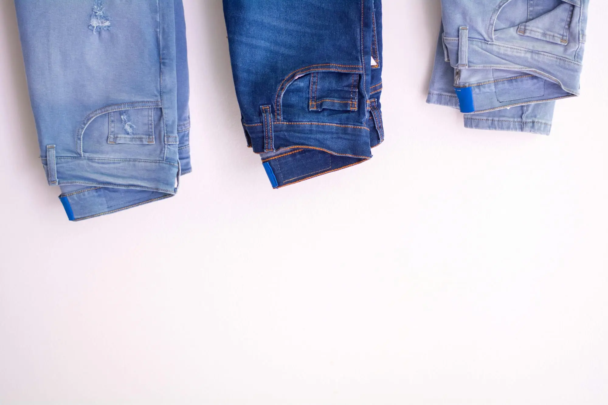 Three pairs of denim jeans hanging on a white wall